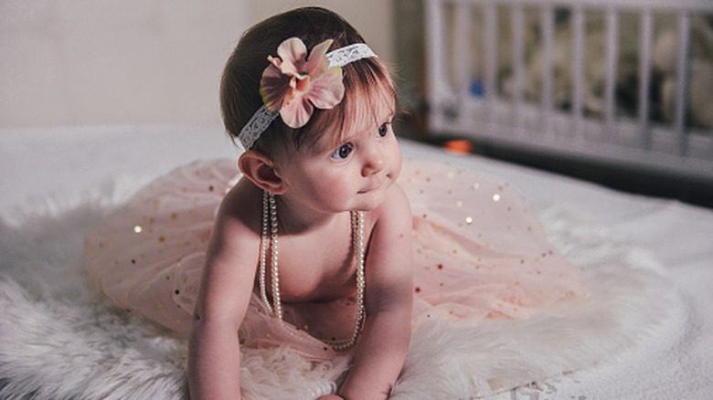 baby looking curiously and wearing a strand of pearls