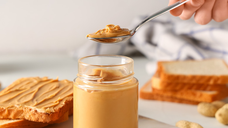 Person scooping peanut butter from a jar for sandwiches