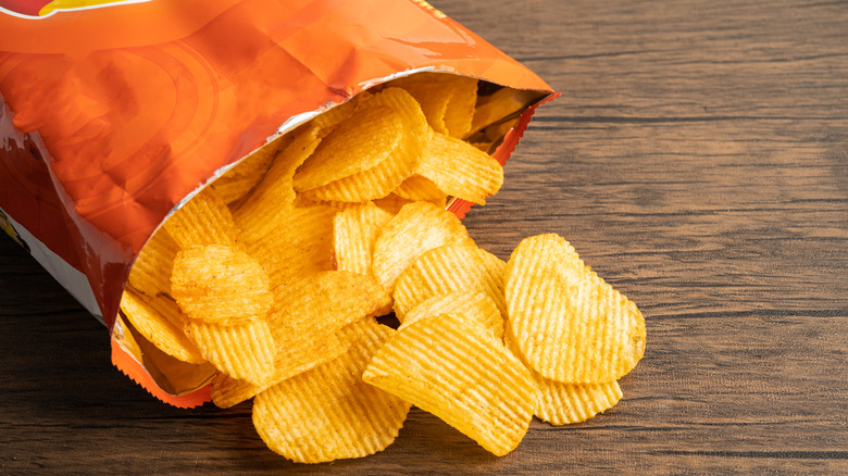 An opened bag of chips spills out onto a wooden table