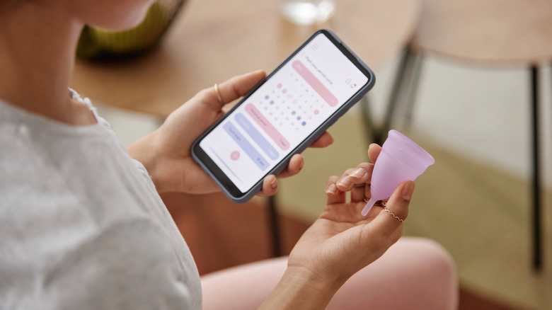 A woman looking at calendar and holding menstrual cup