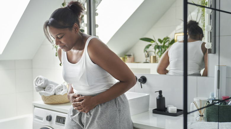 A woman in the bathroom holding her stomach in discomfort