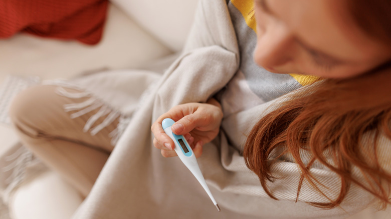 Woman on couch using an oral thermometer