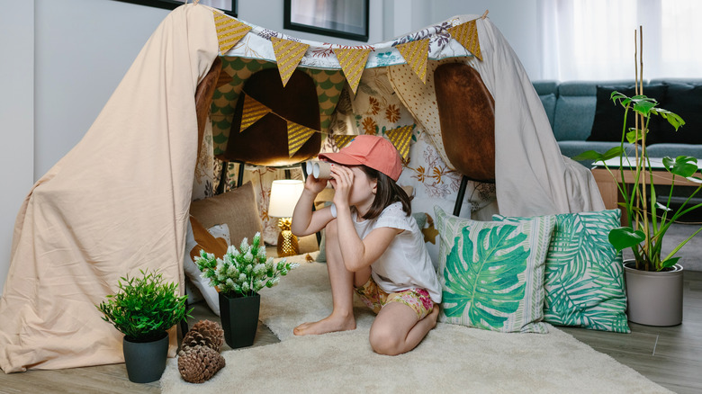 A child sits in a homemade fort made from draped blankets and sheets