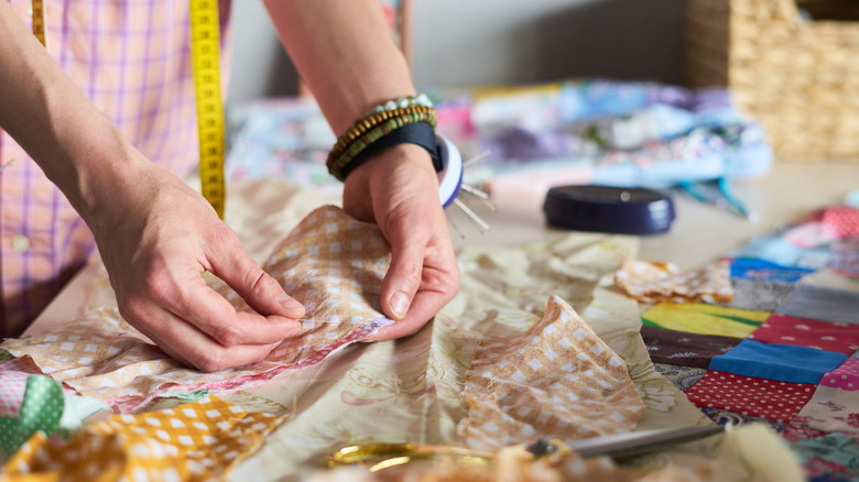 A person holds a piece of fabric with two hands, with one hand placing a needle through the fabric