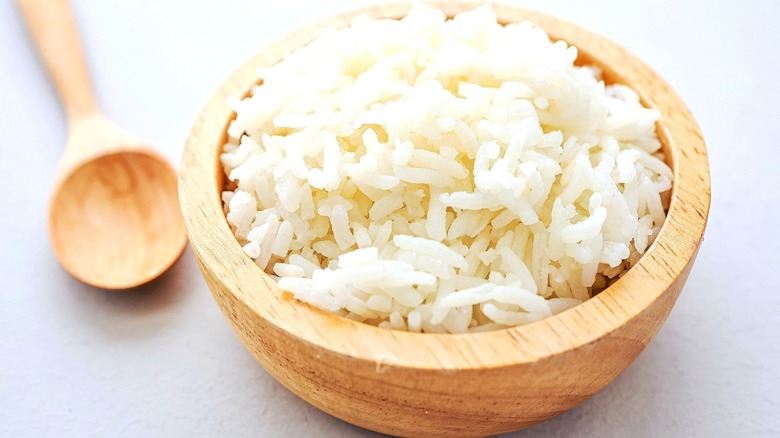 Cooked white rice in a small wooden bowl next to a wooden spoon