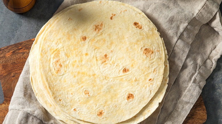 Stack of flour tortillas on a folded kitchen towel over a wooden serving board