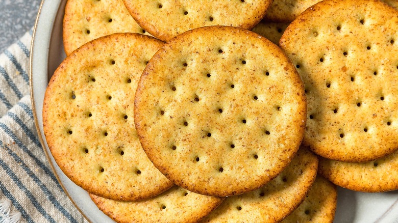 Close-up of round, whole-grain crackers on a gold-rimmed plate over a folded, striped cloth napkin