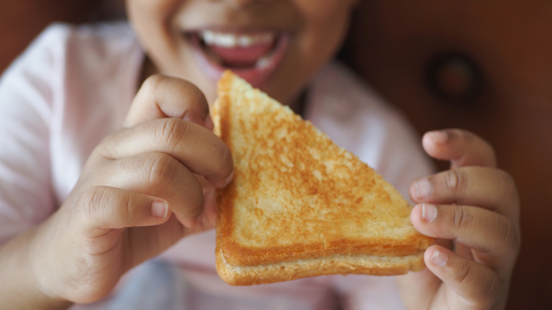 Smiling child holding a grilled cheese in both hands