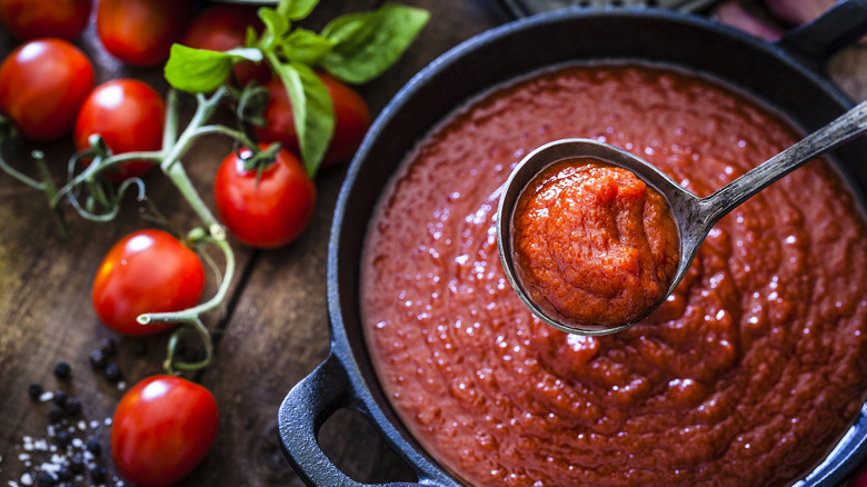 Pot of marinara sauce with a ladle hovering above it and tomatoes to the side