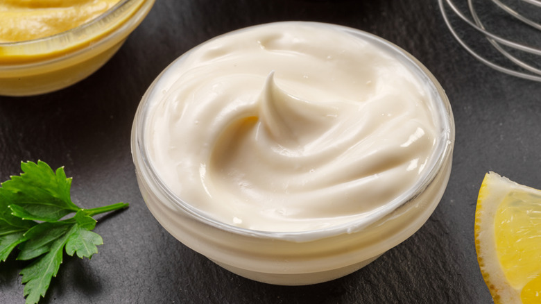 Glass dish filled with mayonnaise with a garnish and a lemon next to it