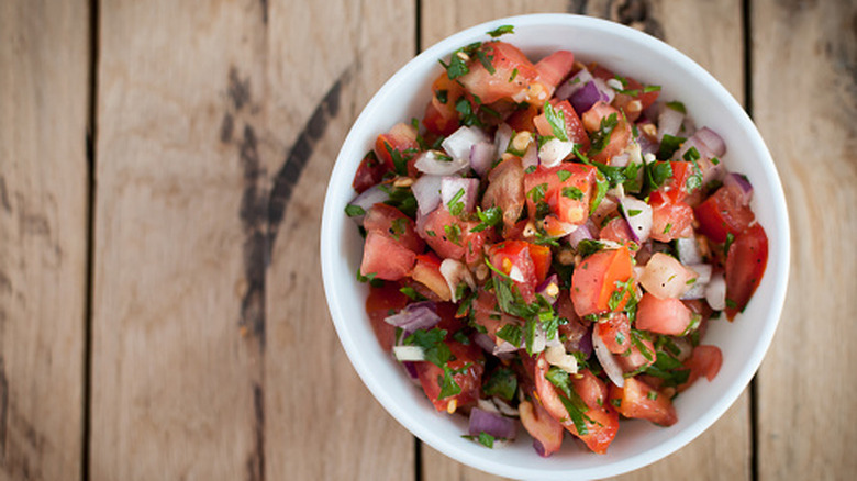 Bowl of salsa made with tomatoes, onions, and seasoning on top of a wooden surface