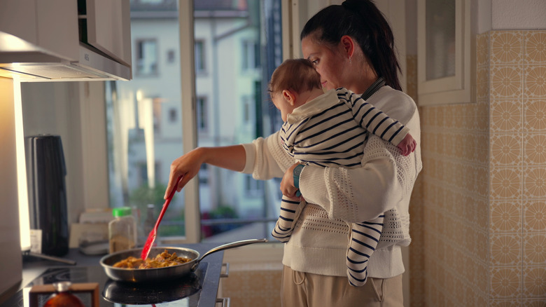 Woman cooking while holding a baby