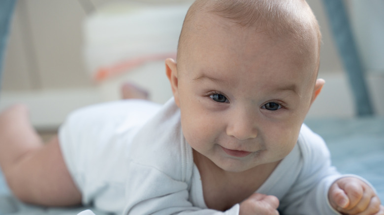 Baby in white onesie laying on stomach