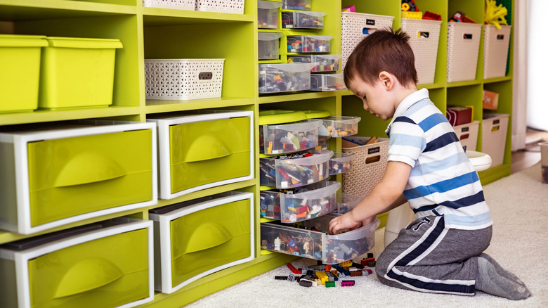 little boy tidies up lego in a well-organized playroom