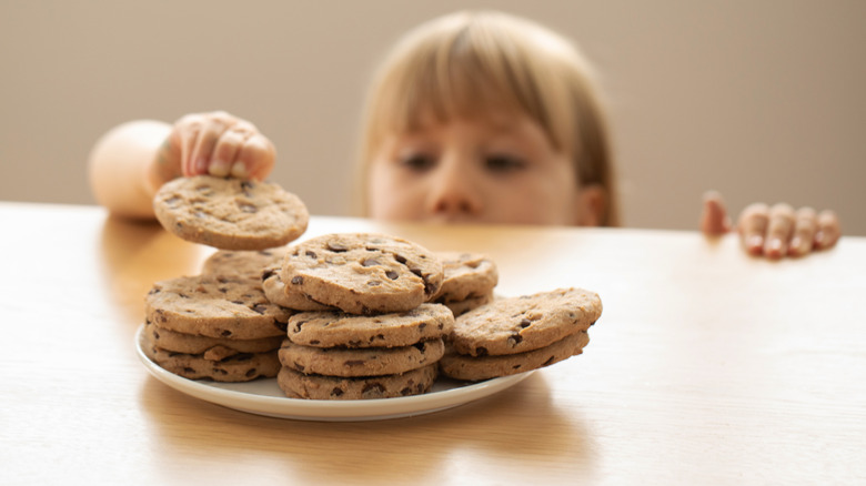 Child reaching over the counter for a chocolate chip cookies