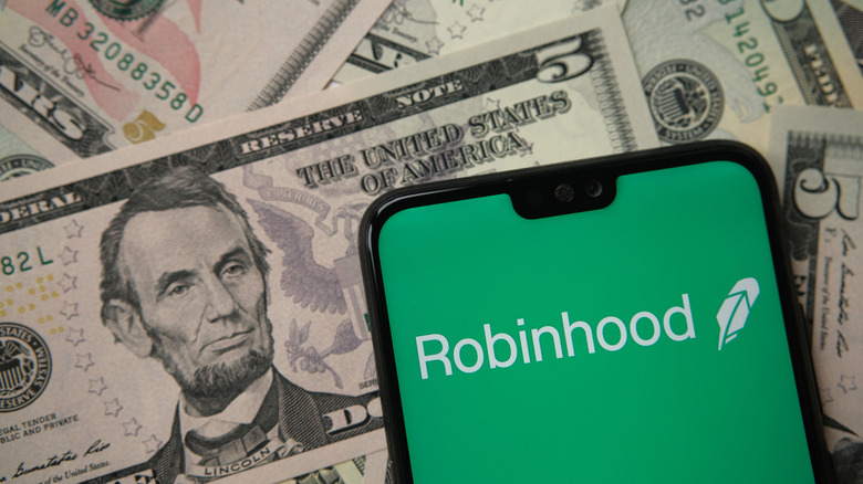 Robinhood Trade and Investments logo on a phone screen with money in the background