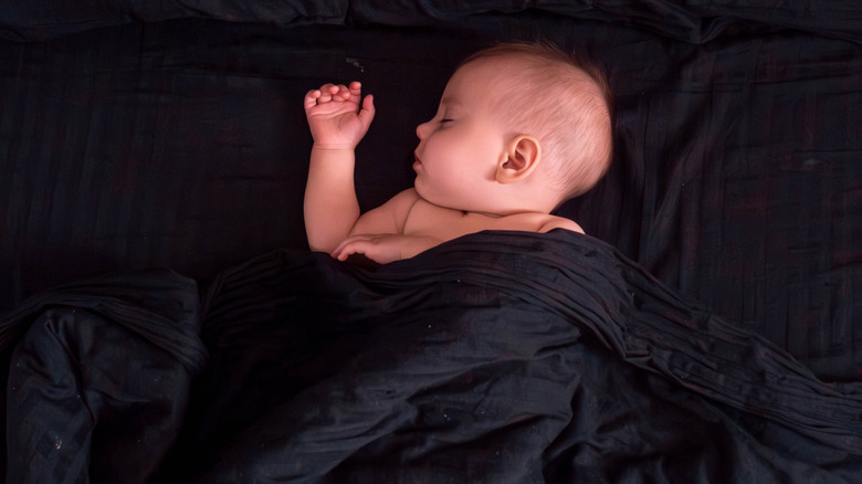 Baby lying on black sheets with a black blanket