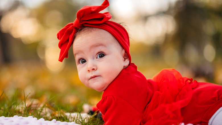 Baby girl in red dress and hair bow lying outdoors
