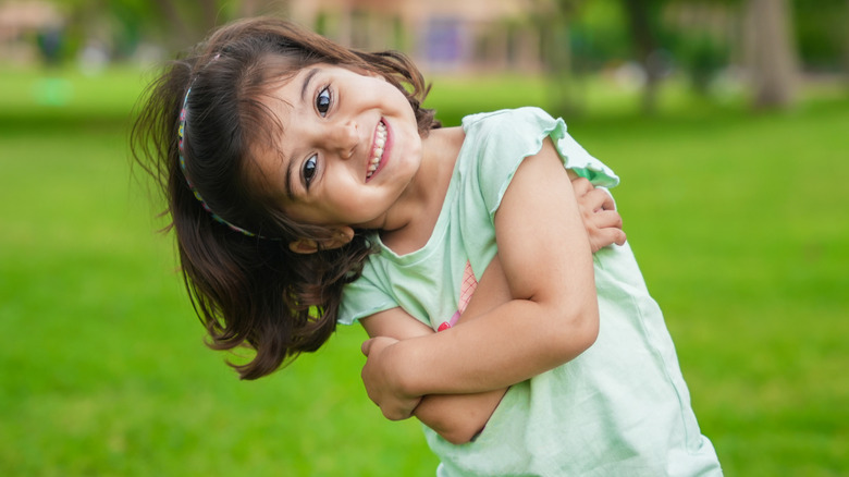 Smiling girl in green shirt leaning sideways and hugging herself