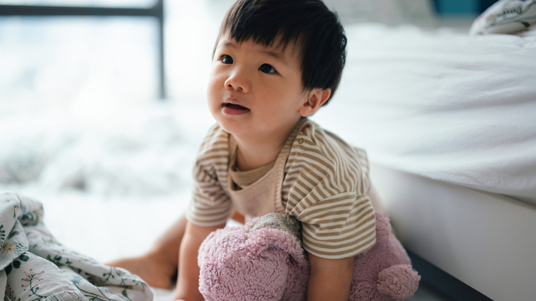 Asian baby on bed with pink stuffed animal
