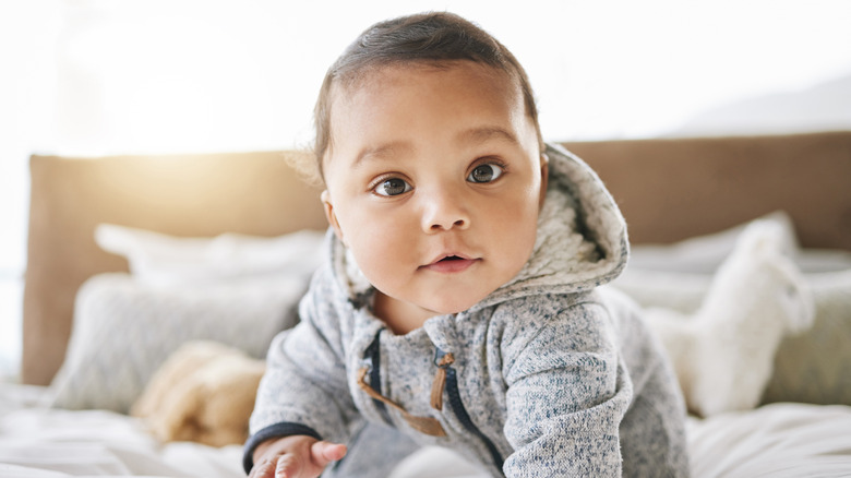 Baby in gray hoodie crawling across bed