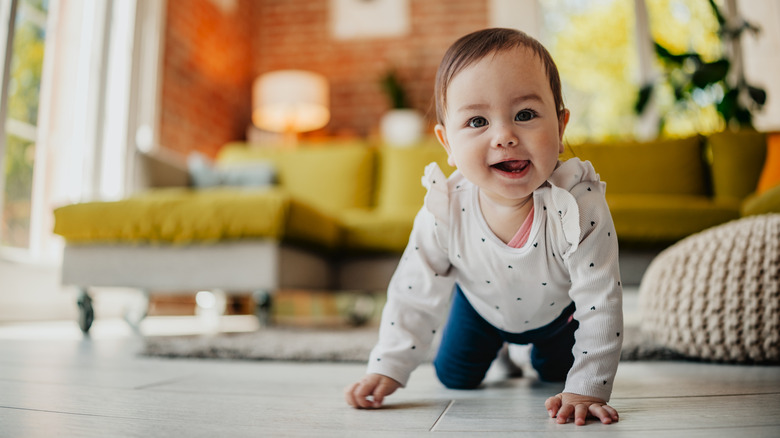 A baby girl crawls on the floor and looks at the camera