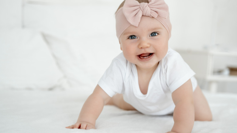 A baby girl wearing a pale pink bow headband looks at the camera