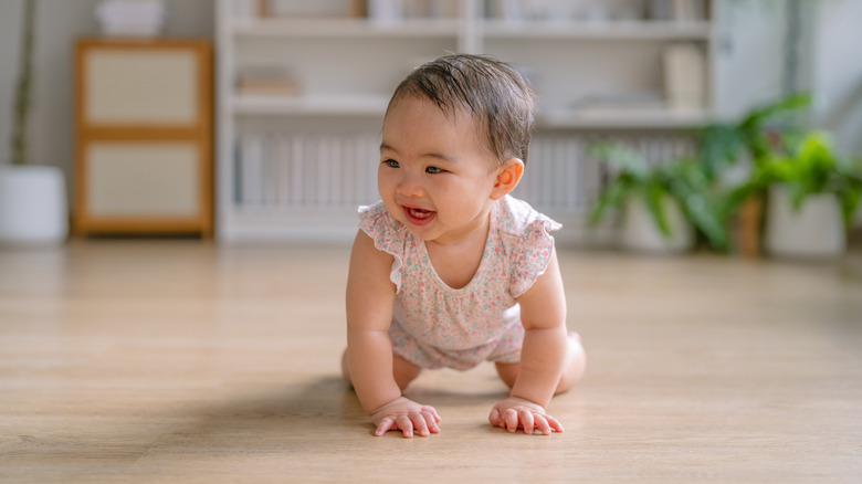 A baby crawls on a hardwood floor, smiling