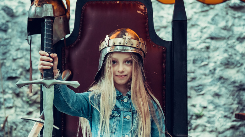 Young girl pretending, wearing a knight's helmet and holding a sword sitting on a throne