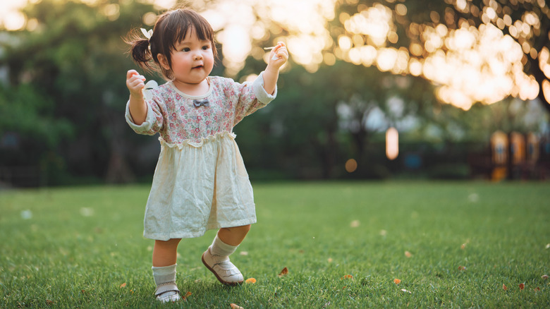 Toddler girl walks in a field with her arms raised