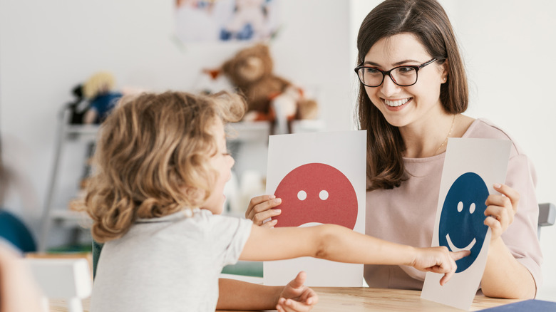 A woman holds up signs depicting emotions and a child points to one of them