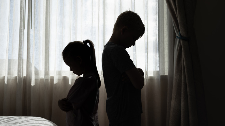 The silhouette of two children standing back to back with their arms folded and their heads down
