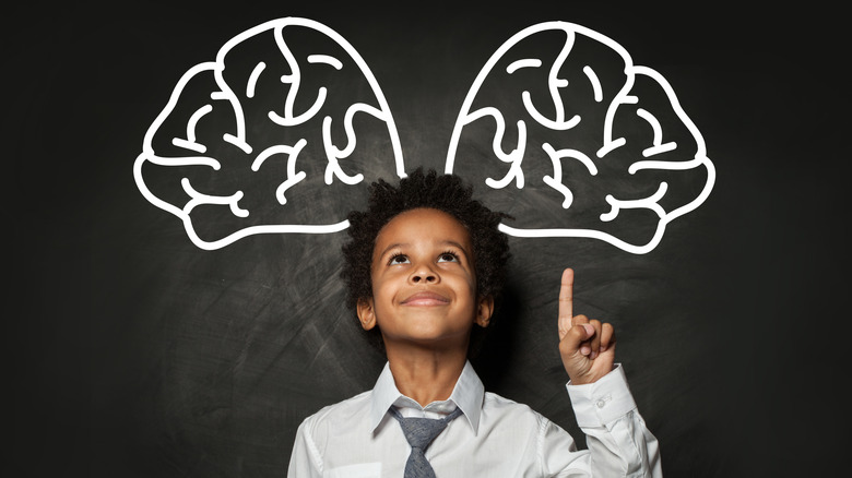 A child points upward toward a drawing of two brains hovering above his head