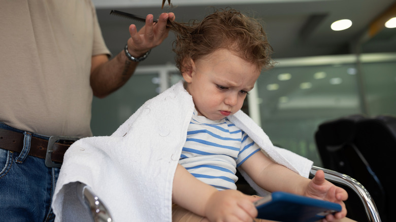 Boy watching tablet while getting his hair cut