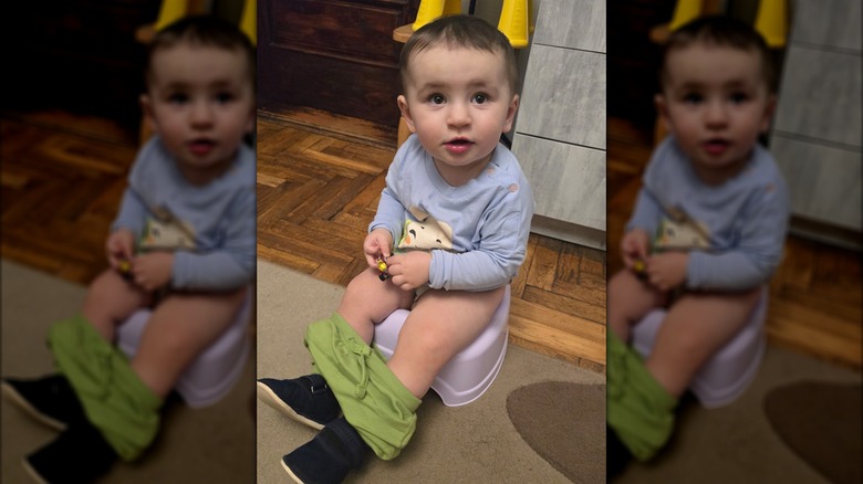 Child in lavender shirt and green pants sitting on potty chair