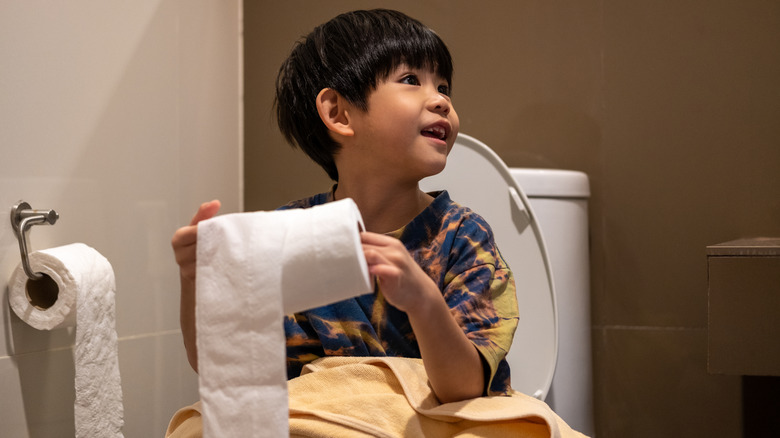 Boy sitting on toilet with roll of toilet paper