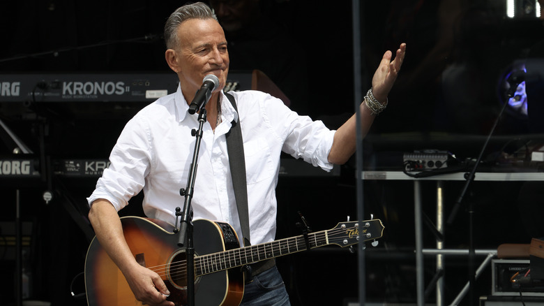 Bruce Springsteen with guitar raising arm at dedication of Obama Library