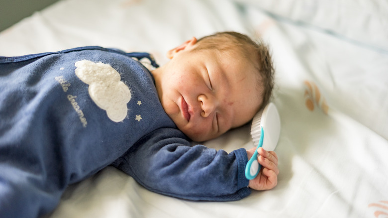 Baby sleeping with a hairbrush in his hand