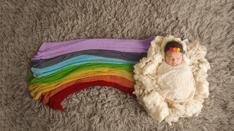 baby swaddled on a cloud blanket with a rainbow fabric next to her