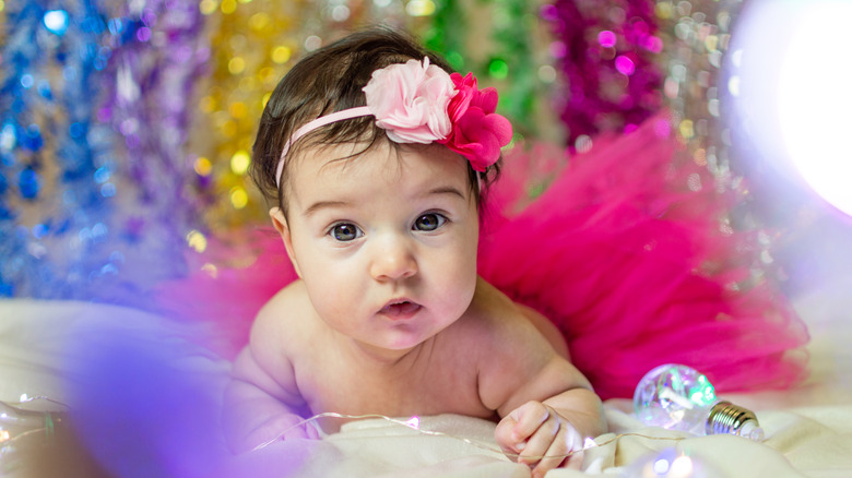 Baby with a pink tutu and bows in front of a sparkly background