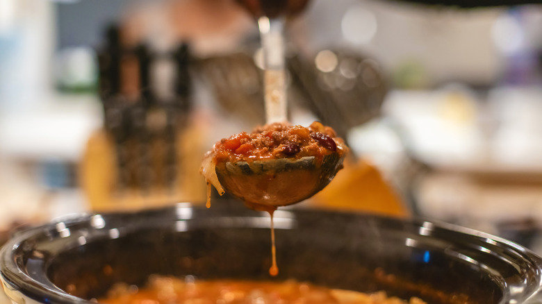 A metal ladle filled with soup ingredients being lifted out of a crockpot