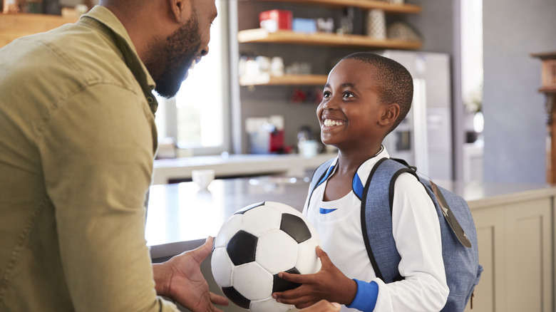 Father speaking to son in the kitchen as the son holds a soccer ball