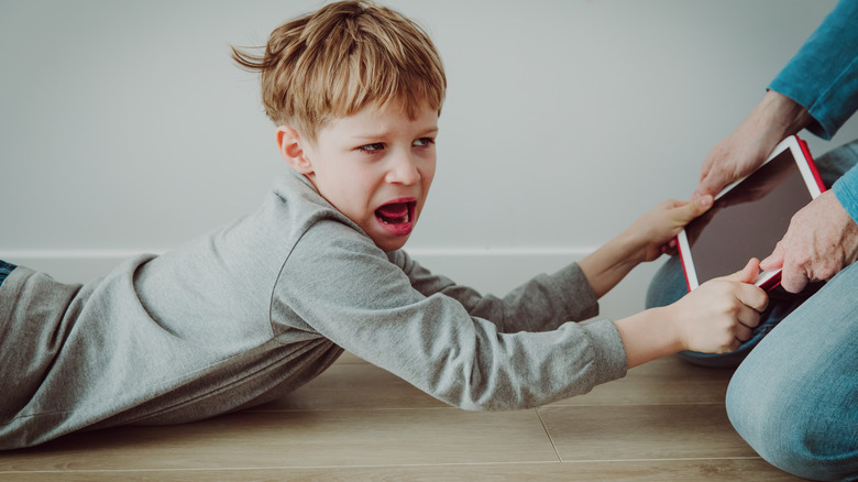Upset child grabbing ipad from parent