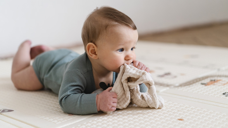 Baby on his tummy chewing on a cloth
