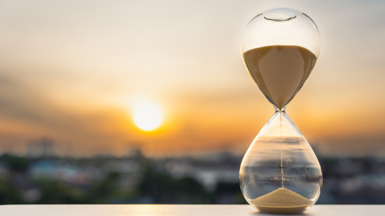 Sand pouring through an hourglass that sits on an open-air countertop with a blurred sun and cityscape in the background