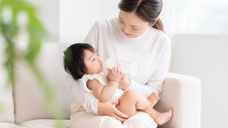 young mom feeding infant while sitting on a sofa