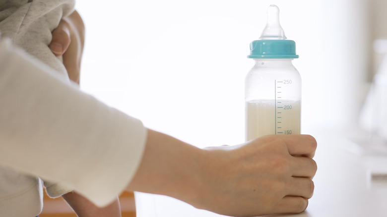 woman reaching for a baby bottle to feed an infant