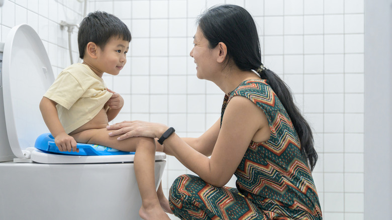 Asian mother with toddler boy sitting on toilet