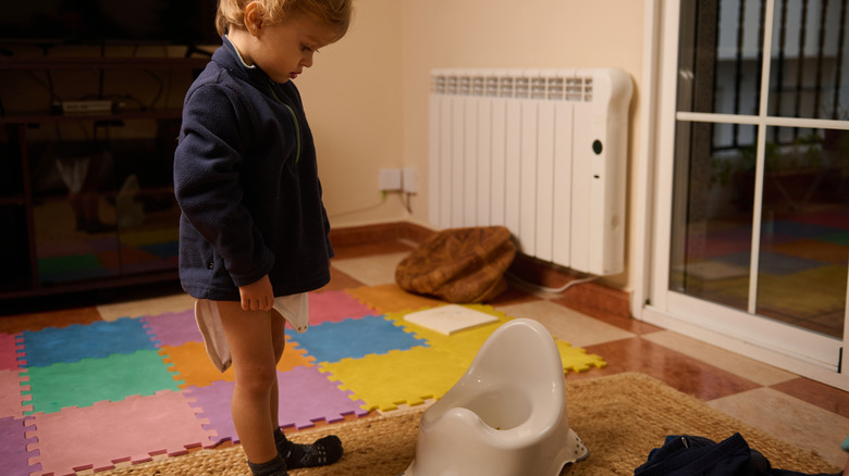 Toddler boy looking at potty training chair