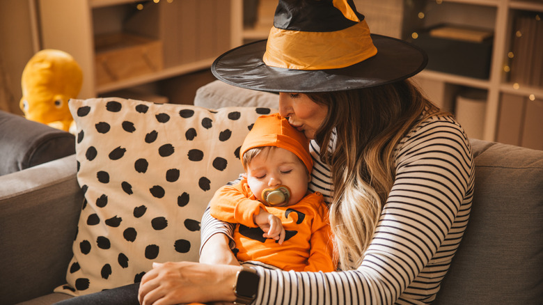 Mother in a witch hat comforting baby in pumpkin costume